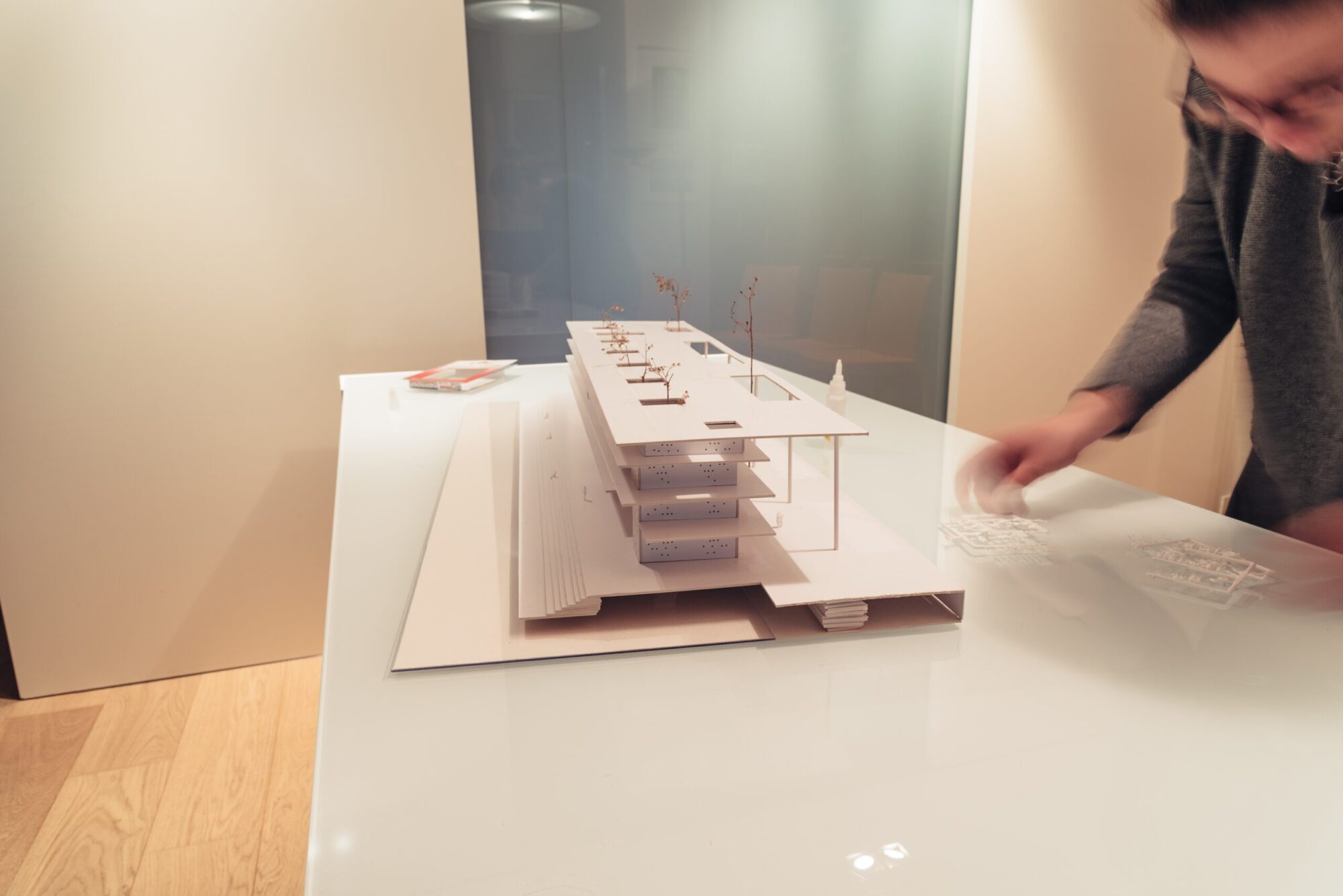 A designer assembling a scale model of a modular trade show booth with layered structures and intricate details.
