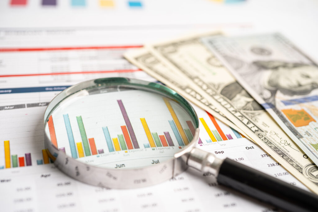 Magnifying glass on data charts graphs paper with US dollar banknotes